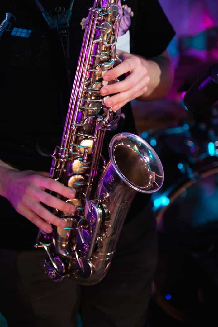 Musician playing saxophone with colorful stage lights adding vibrant ambiance, focusing on hands and instrument.